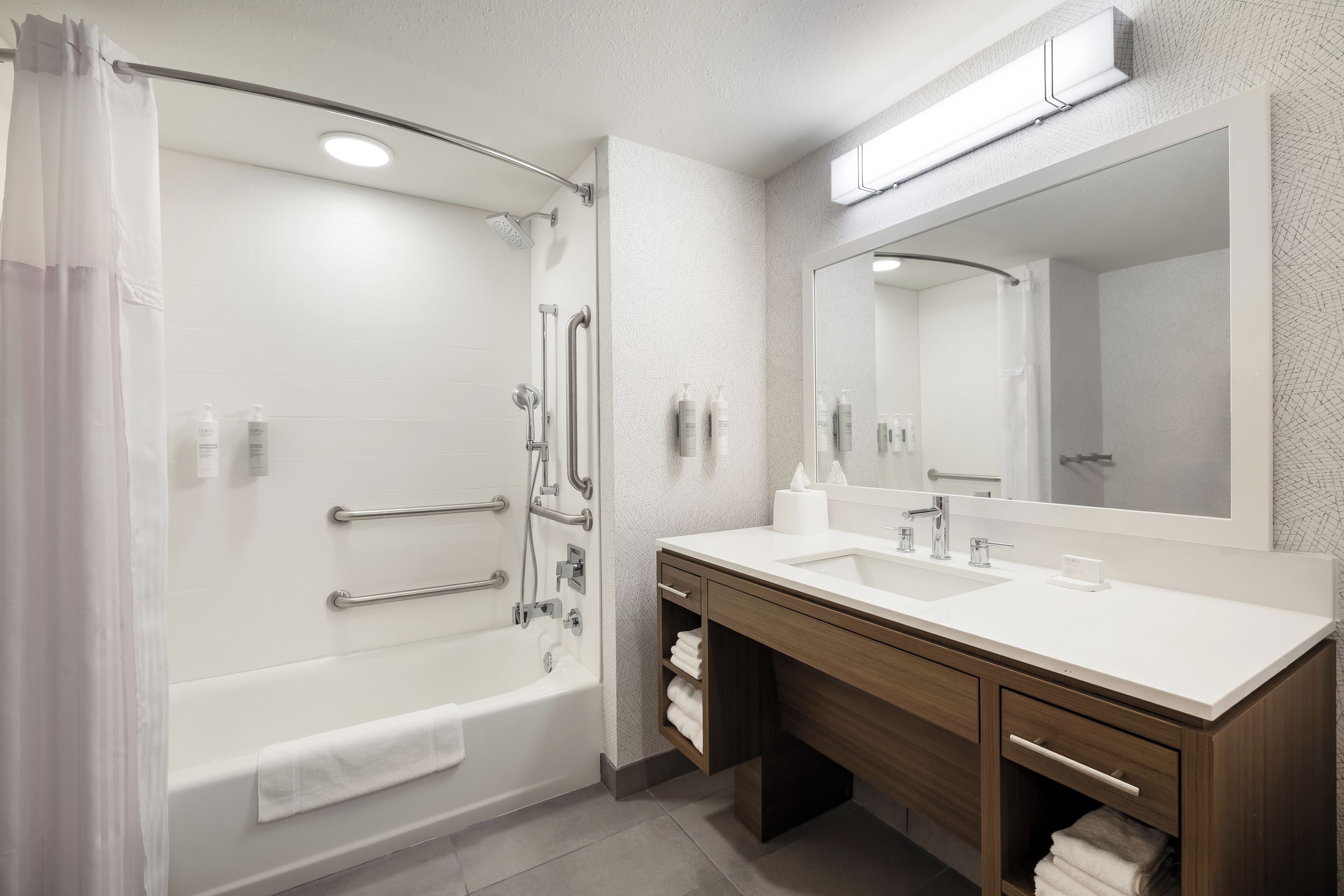 A modern bathroom with a bathtub, shower, vanity, and a large mirror.