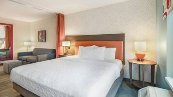 Una habitación de hotel con una cama grande, un sofá, una mesita de noche con lámpara, un espejo y un papel tapiz estampado.