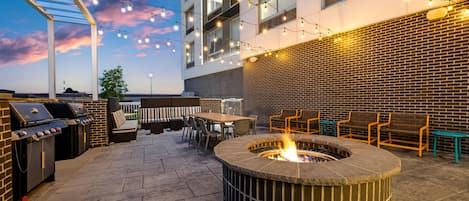 An outdoor patio area with a fire pit, seating, and a grill.