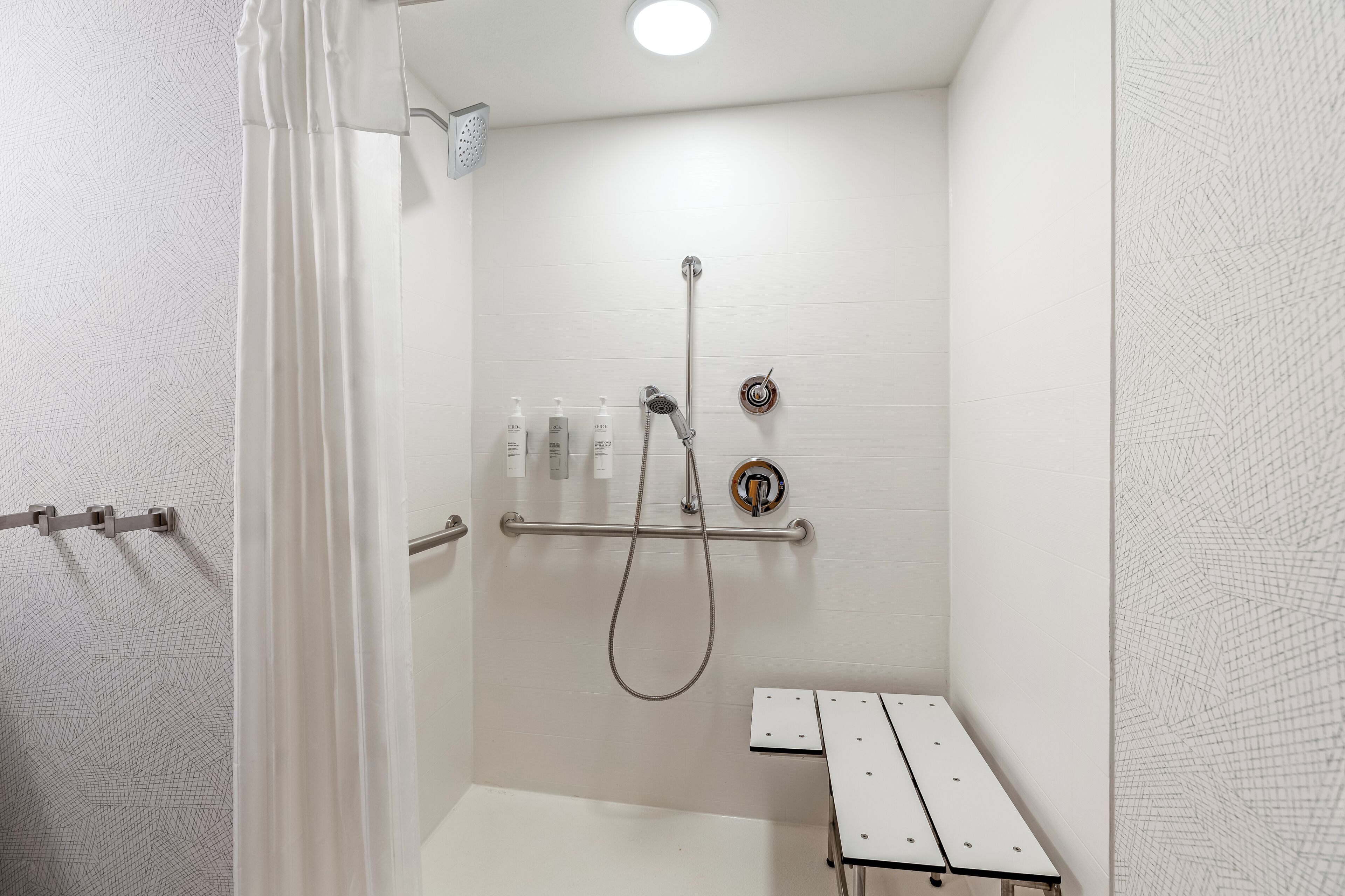 A white bathroom with a shower, a towel rack, and a bench.