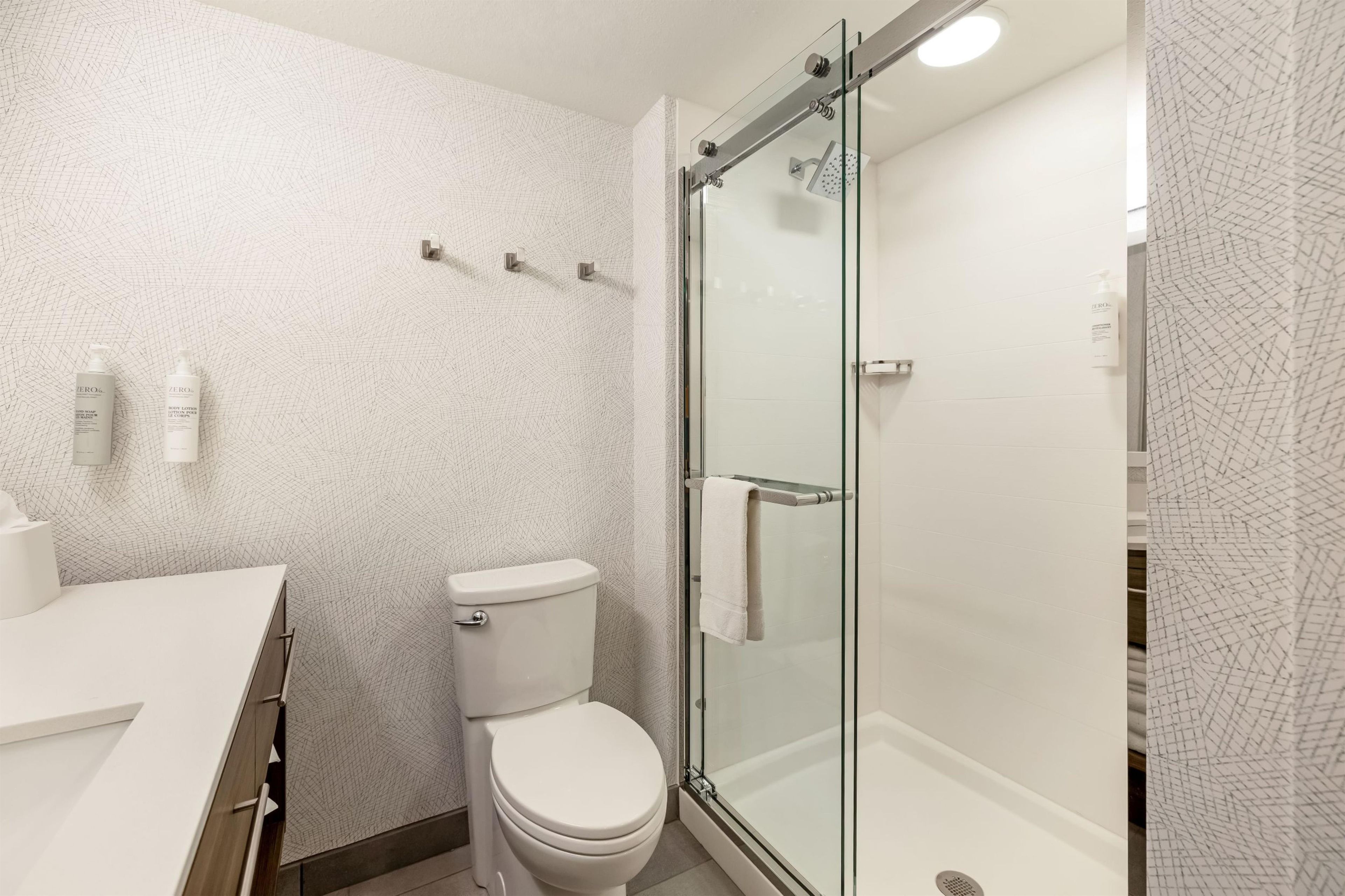 Un baño moderno con ducha envuelta en vidrio, inodoro y lavamanos blancos.