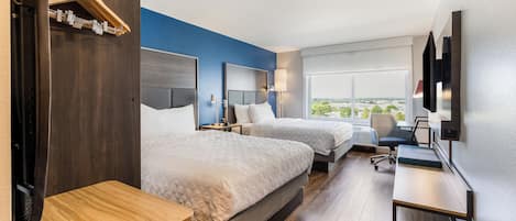 A hotel room with two beds, a desk, a chair, a TV, and a large window with a view.