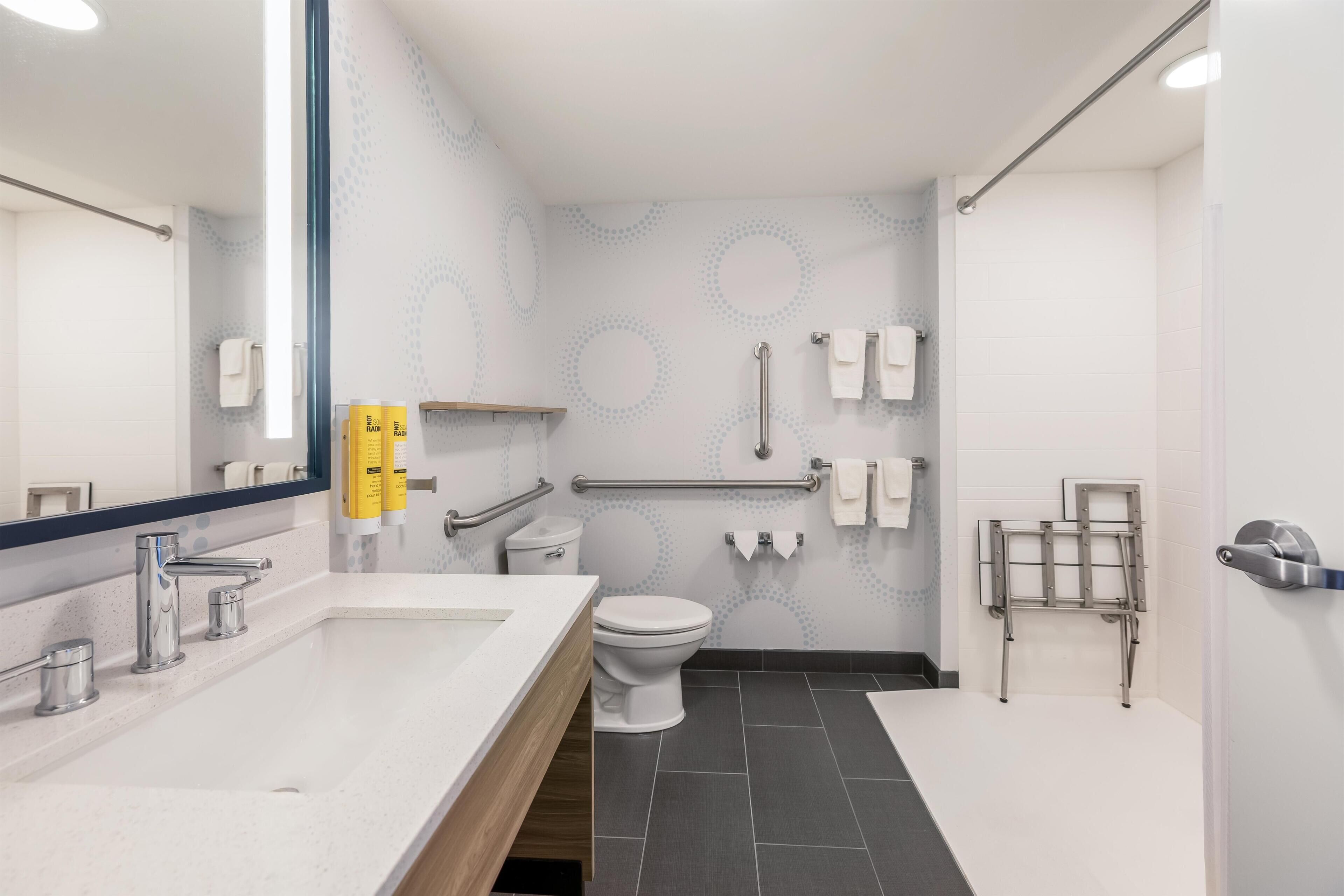 A modern bathroom with a white sink, a toilet, a shower area, and a handrail.