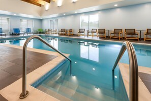 An indoor swimming pool with clear water, surrounded by lounge chairs and tables, and large windows providing natural light. - Tru By Hilton Madison East (Madison)