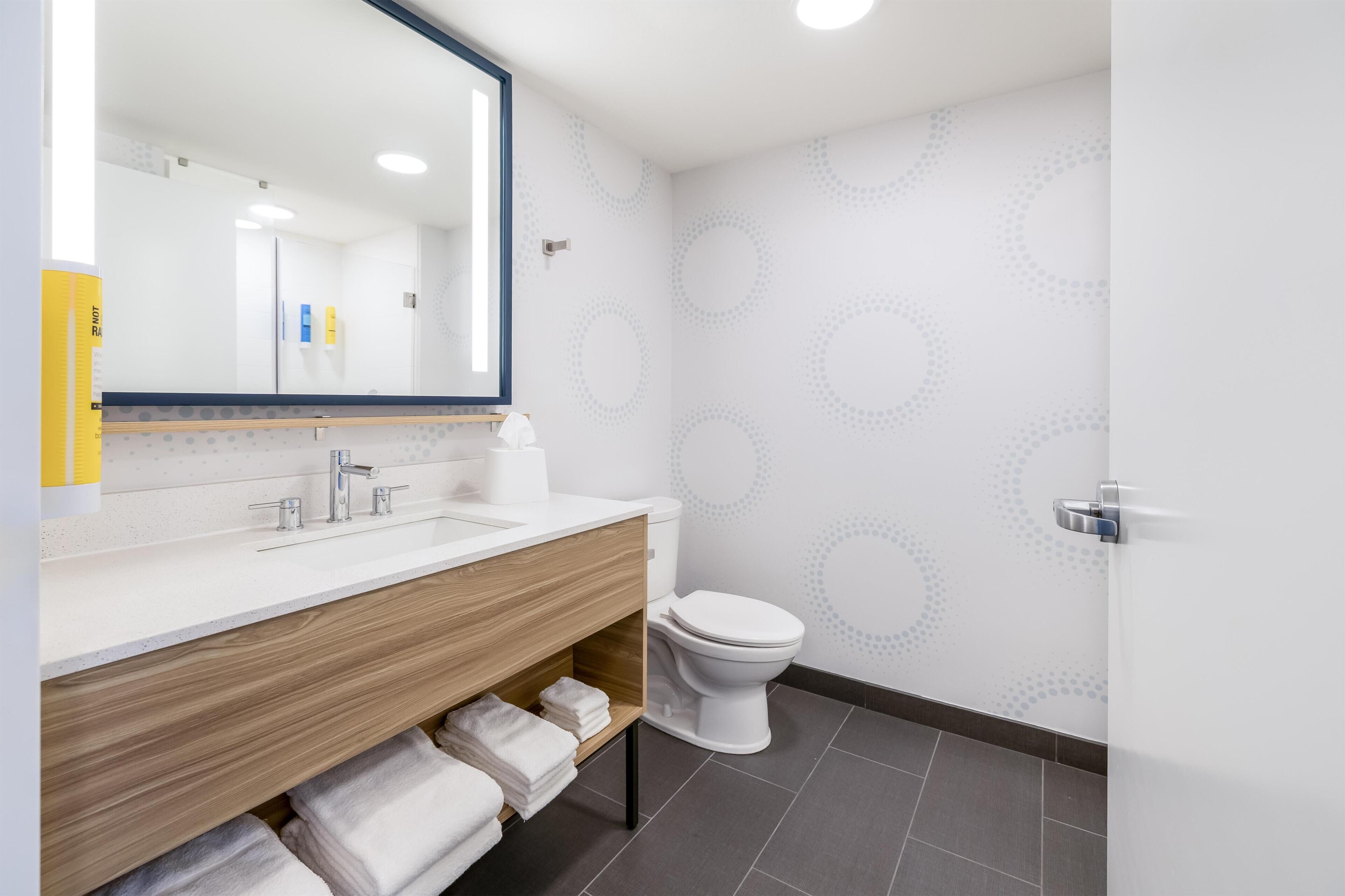 A modern bathroom with a wooden vanity, a white toilet, and a large mirror.