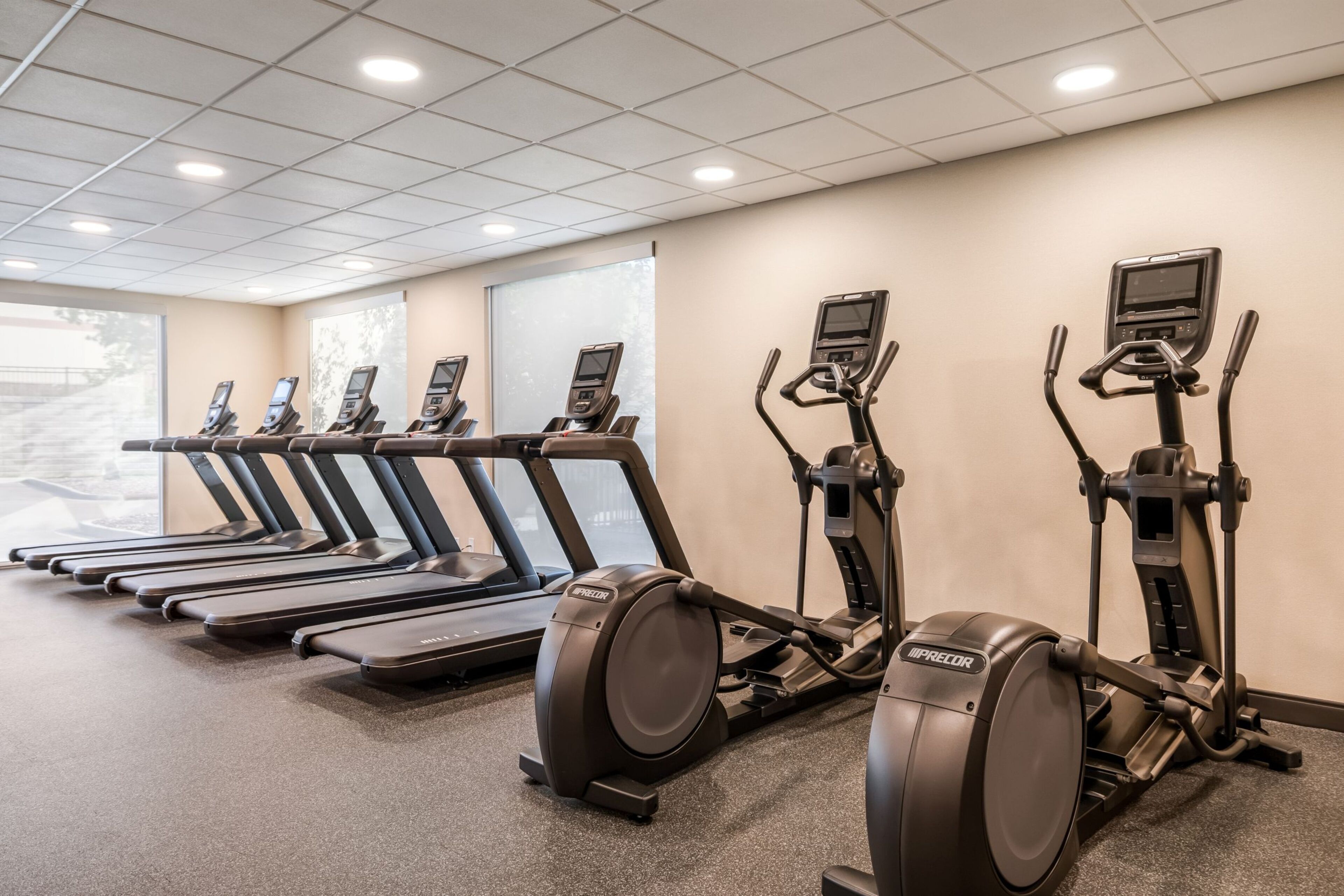 Een sportschool met loopbanden, elliptische trainers en een scherm aan de muur.