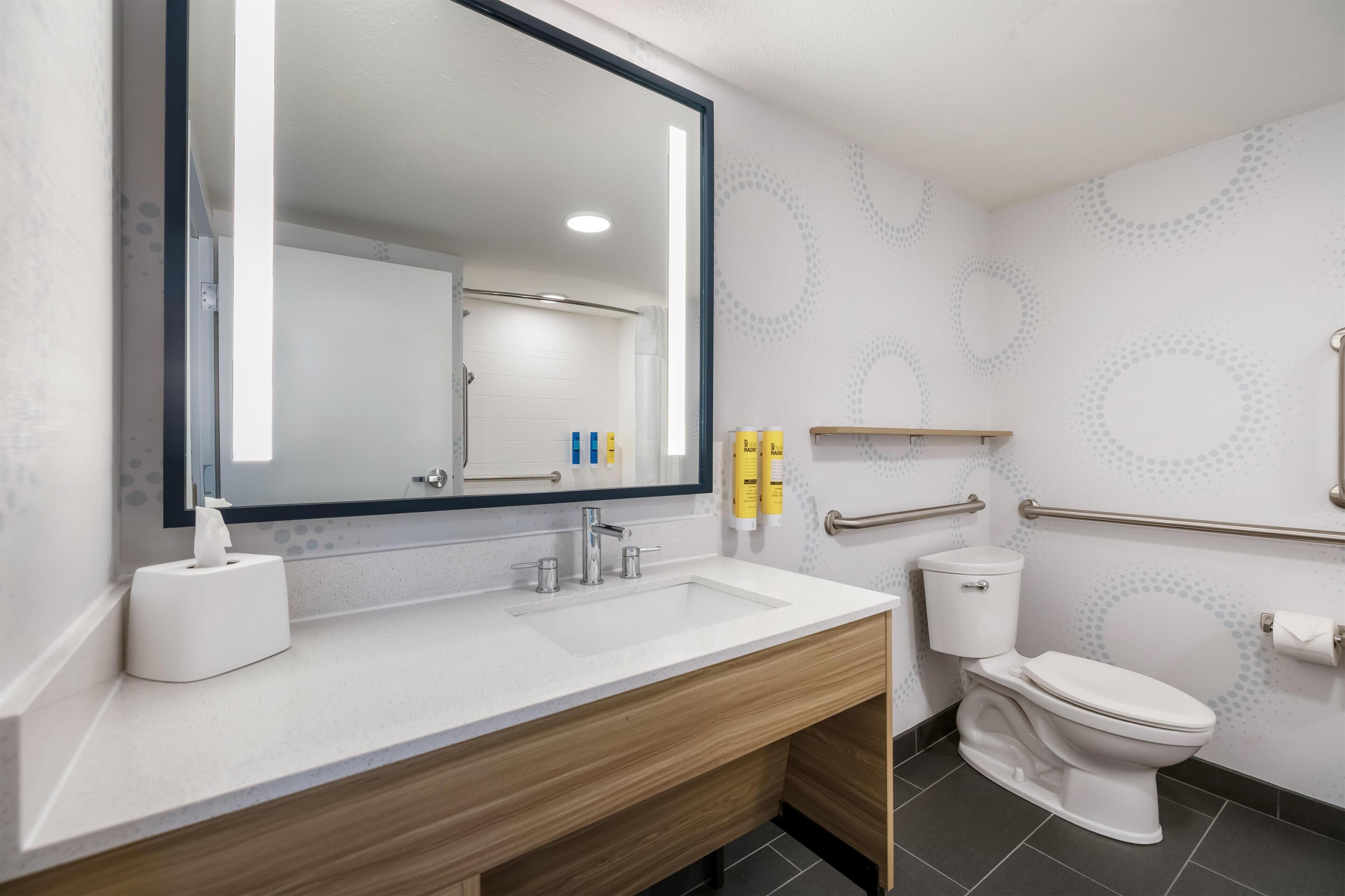 A modern bathroom with a large mirror, a sink, a toilet, and a shower area.