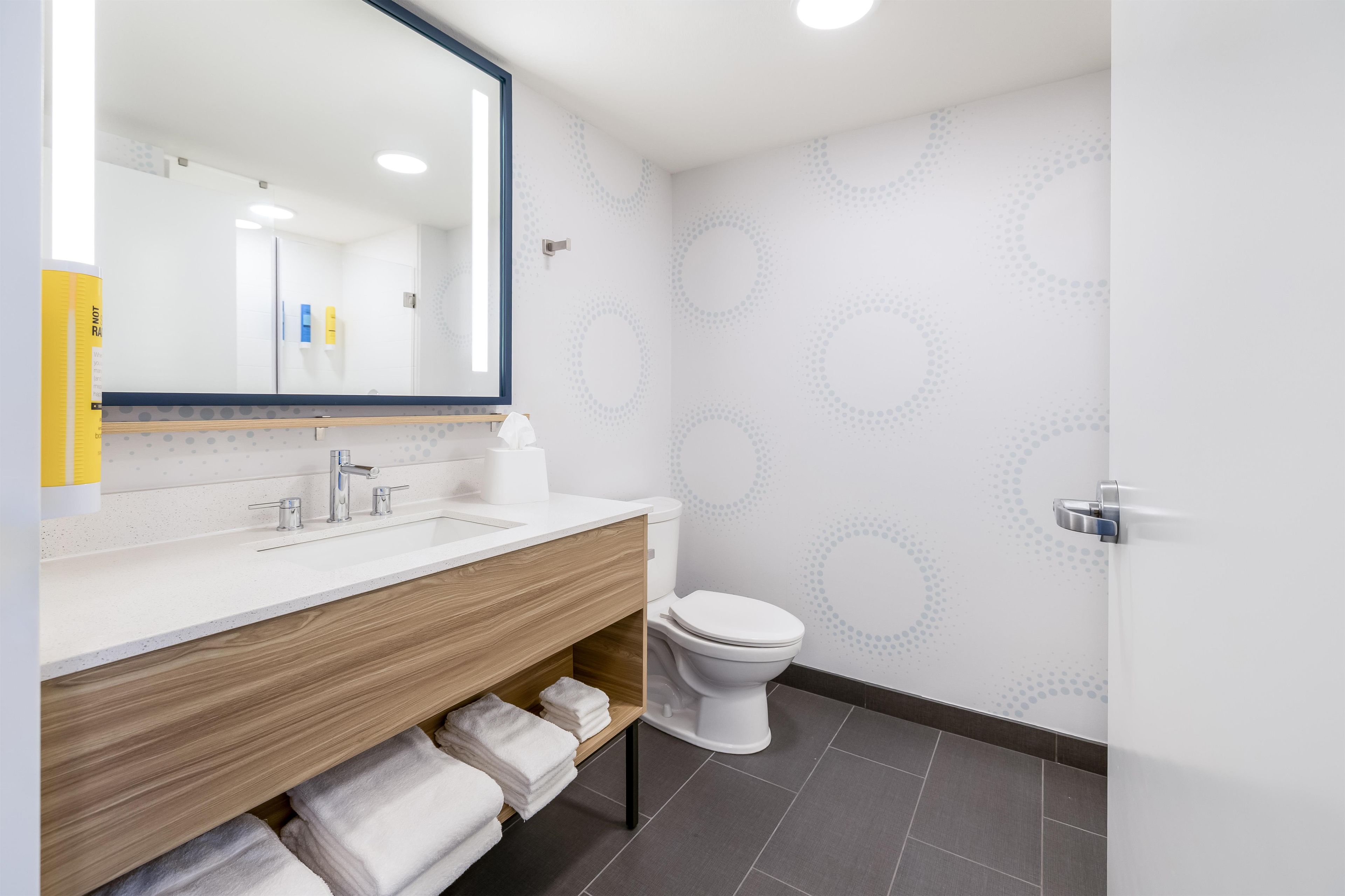 Un baño moderno con tocador de madera, inodoro blanco y espejo grande.