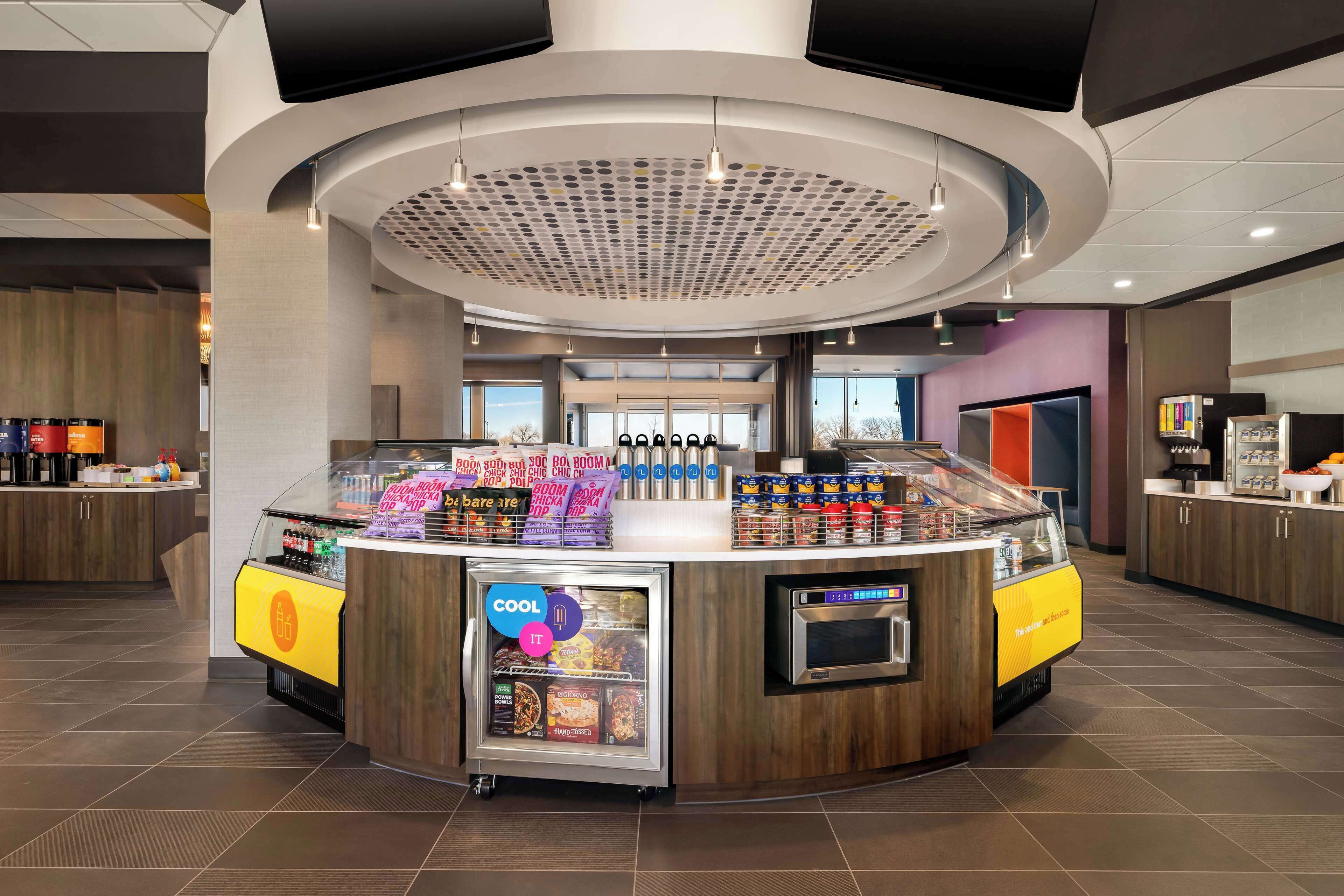 Un patio de comidas moderno con una isla central que tiene un expositor refrigerado y un microondas.