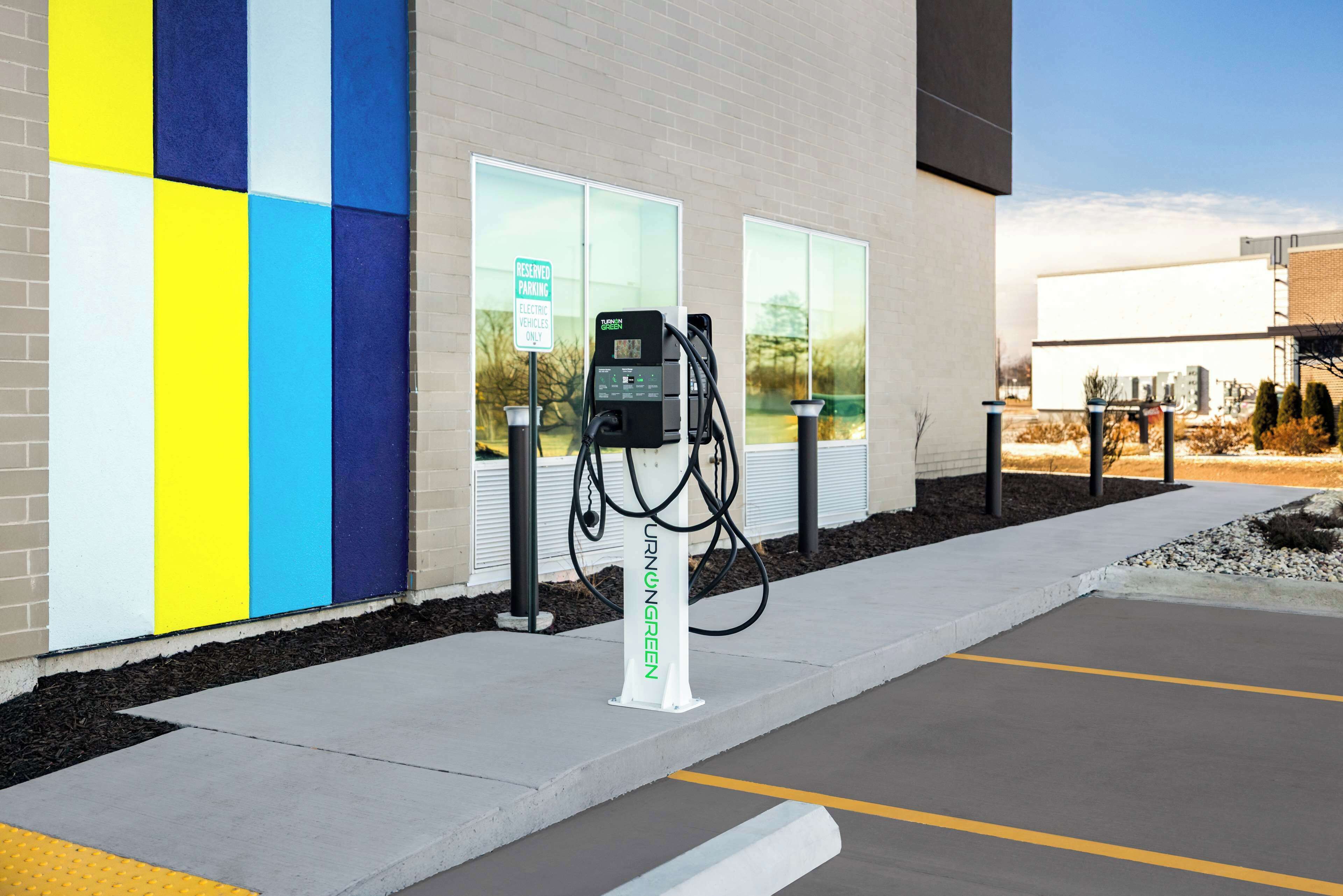 Une borne de recharge pour véhicules électriques se trouve devant un bâtiment dont le mur est peint de couleurs vives.
