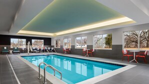 Ein modernes Hallenbad mit klarem, blauen Wasser, umgeben von grauen Fliesenböden und roten Stühlen.