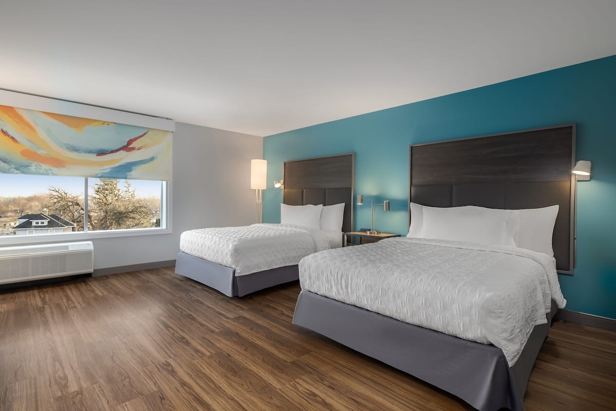 Habitación de hotel con dos camas, un ventanal con vistas y un diseño moderno.