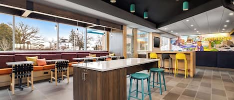 A modern restaurant with a central island, bar stools, and a seating area with a view of the outside.