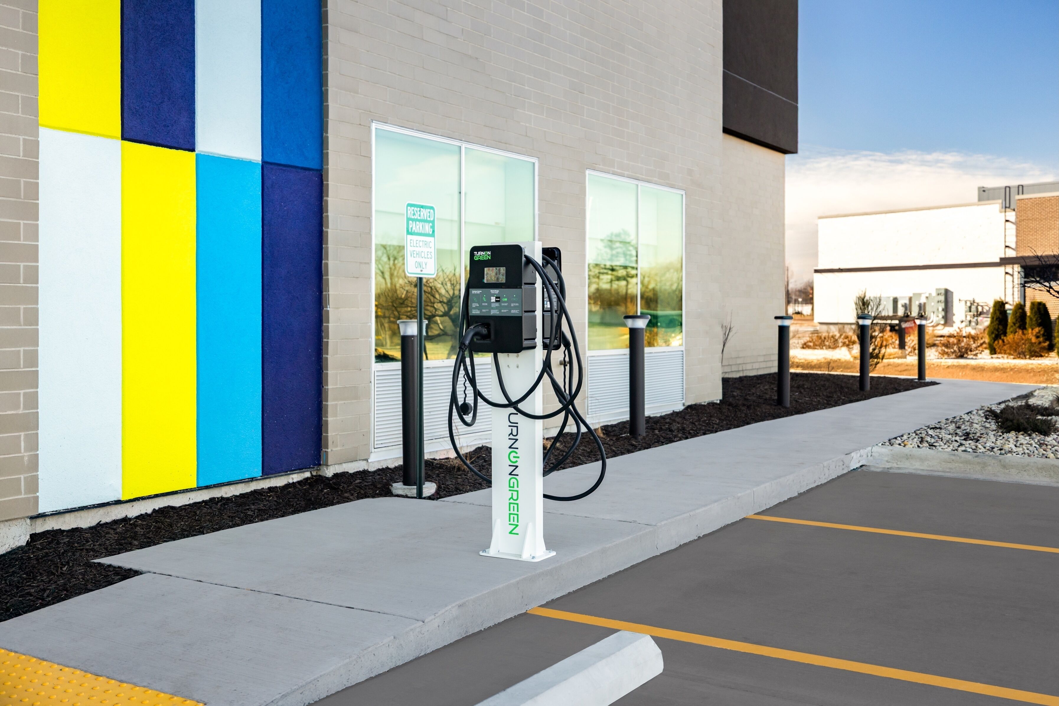 An electric vehicle charging station in front of a building with a colorful wall and a clear sky.