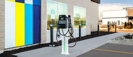 An electric vehicle charging station in front of a building with a colorful wall and a clear sky.