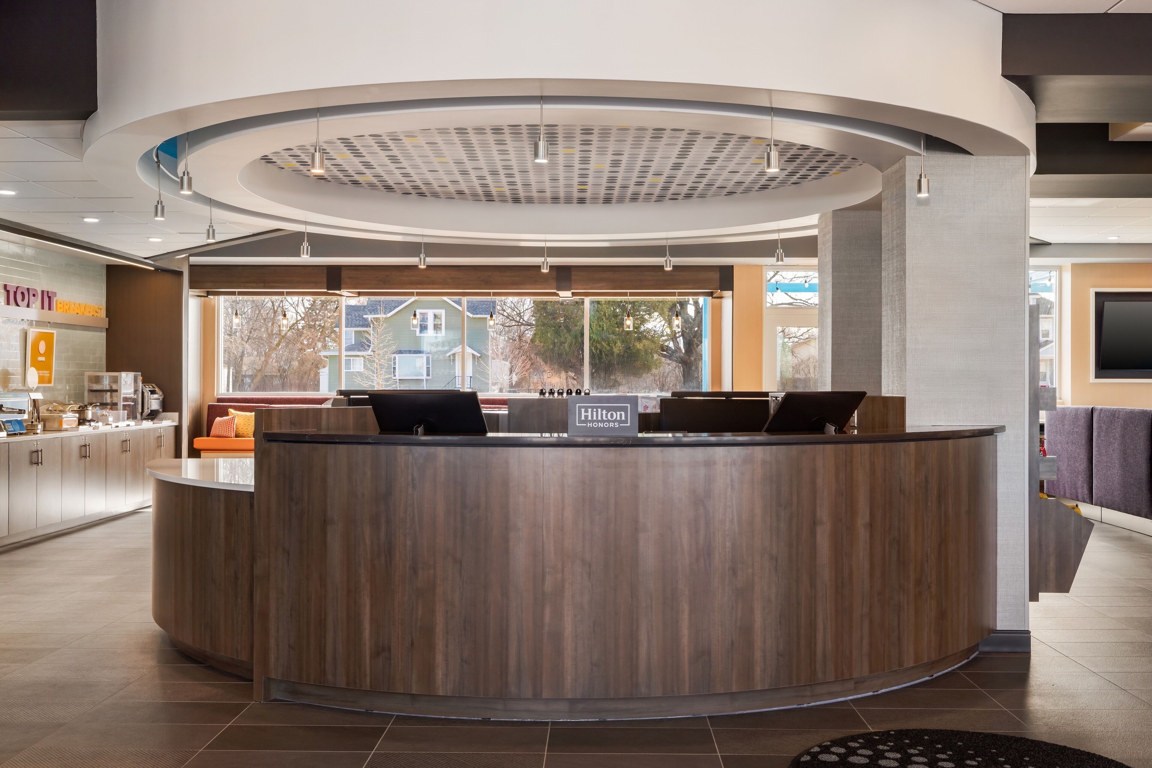 A modern hotel reception desk with a wooden finish, a digital display, and a view of the outside.