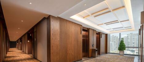 A modern hotel corridor with a patterned carpet, wooden panel walls, and a skylight.