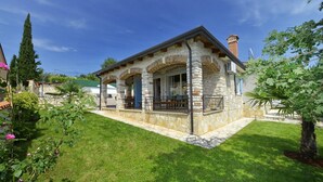 A stone house with a covered patio, surrounded by well-maintained grass and trees. - Villa Dany With View (Kastelir-Labinci)