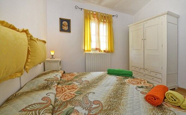 A bedroom with a bed, a nightstand, a radiator, a wardrobe, and a window with curtains. - Villa Dany With View (Kastelir-Labinci)