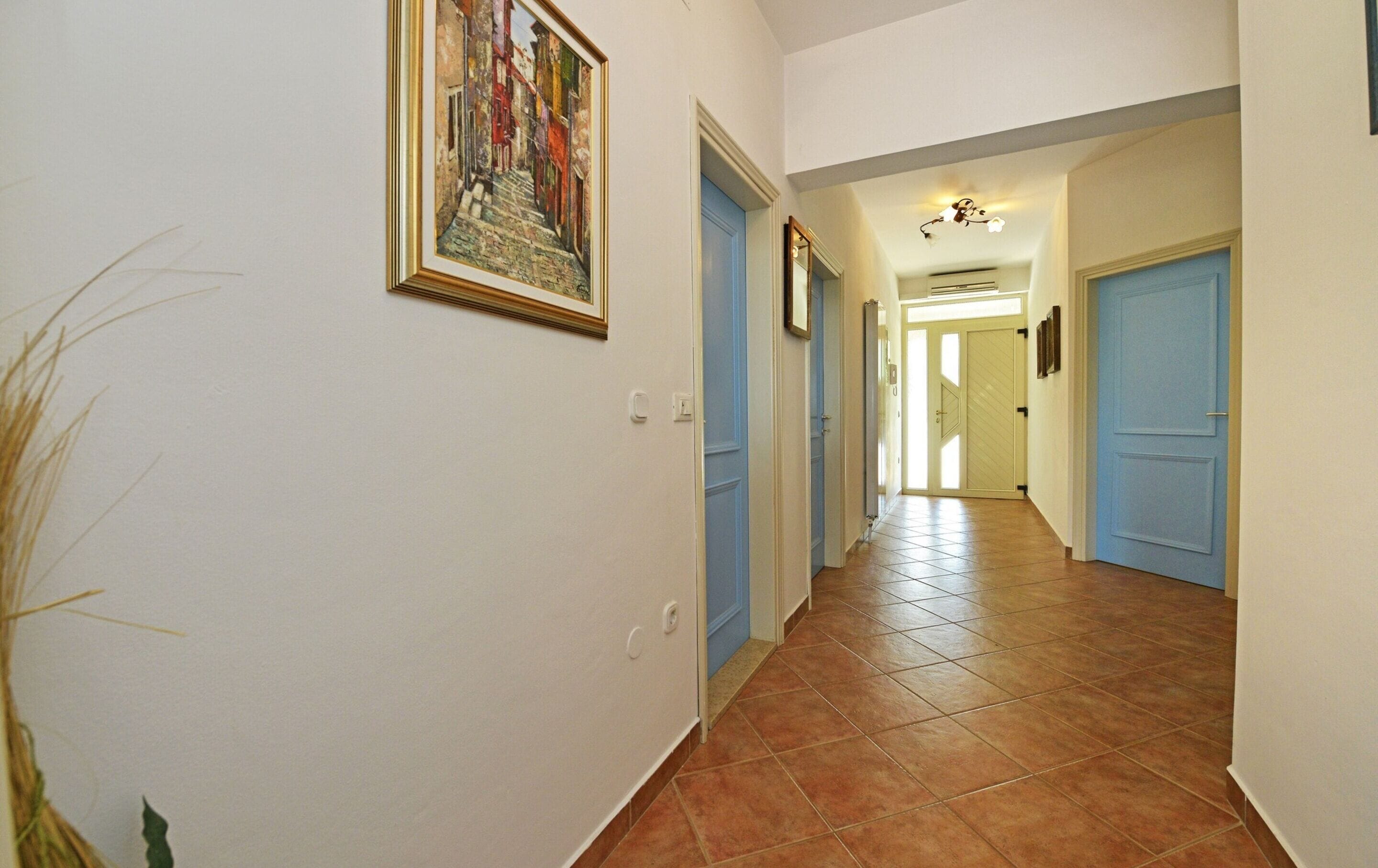 Un couloir avec des portes bleues, un sol carrelé et un tableau encadré accroché au mur.