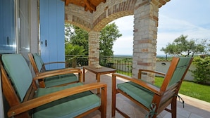 A covered patio with wooden furniture and a stone pillar, overlooking a lush garden and a distant view. - Villa Dany With View (Kastelir-Labinci)