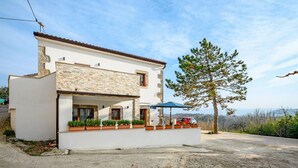 A modern two-story house with a stone facade, a covered porch with potted plants, and a view of the surrounding landscape. - Beautiful Villa in Nature (Groznjan)