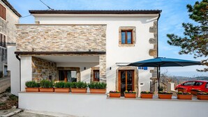 A two-story building with a stone facade, a balcony with potted plants, and a red car parked outside. - Beautiful Villa in Nature (Groznjan)