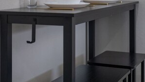 Een strakke eettafel met witte borden en glazen, een kleine potplant en een zwarte stoel.