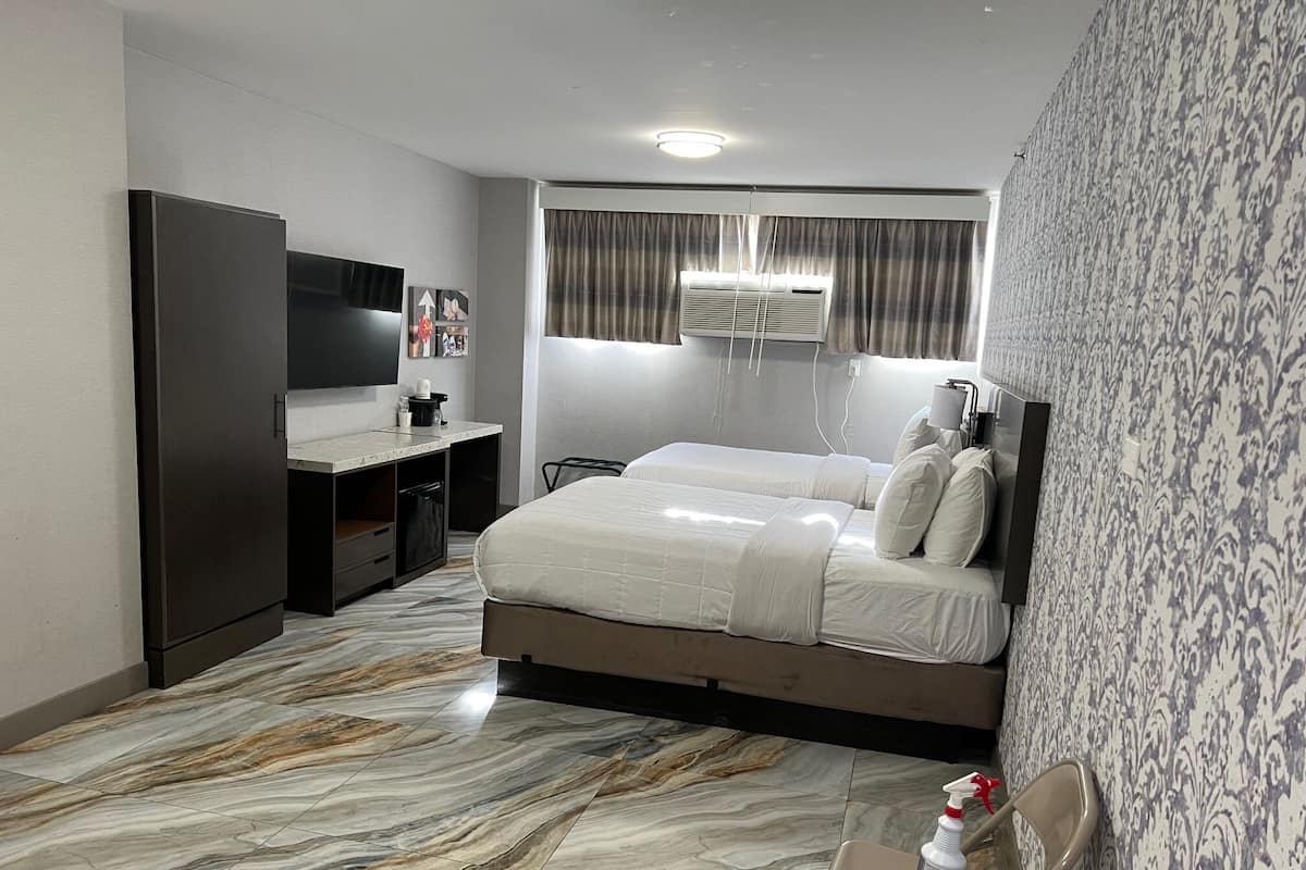 A hotel room with a bed, a desk, a wardrobe, a TV, and a bathroom with a shower.