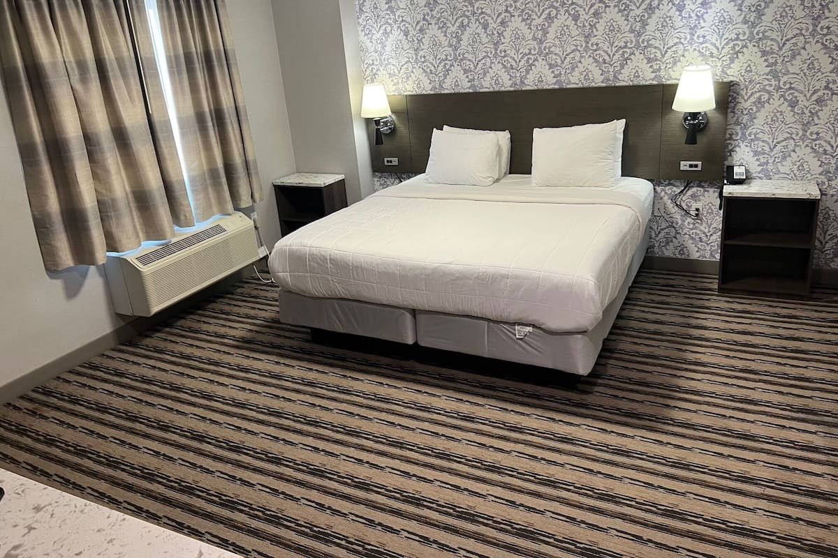 A hotel room with a large bed, two bedside tables with lamps, a radiator, and patterned wallpaper.