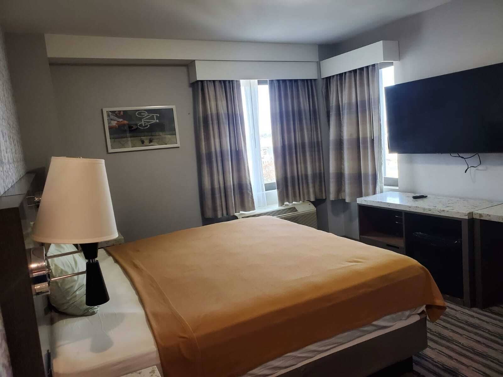 A hotel room with a bed, a desk, a television, and a window with curtains.
