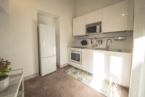 Une cuisine compacte avec des meubles blancs, un four encastré, un four à micro-ondes et un évier.