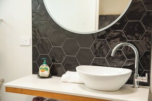 Une salle de bain avec un lavabo blanc, un miroir et un pare-chocs mural en carreaux noirs hexagonaux.