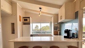 A modern kitchen with a central island, bar stools, a microwave, and a coffee machine. - Driftwood Retreat - Tutukaka (Tutukaka)