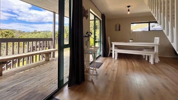 A spacious room with a large sliding glass door leading to a balcony, a white table, and a chair. - Driftwood Retreat - Tutukaka (Tutukaka)