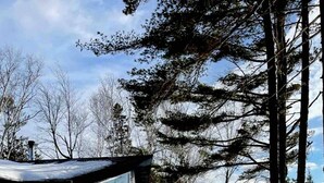 Un bain à remous installé dans un décor extérieur enneigé, avec une terrasse en bois et un petit bâtiment en arrière-plan.