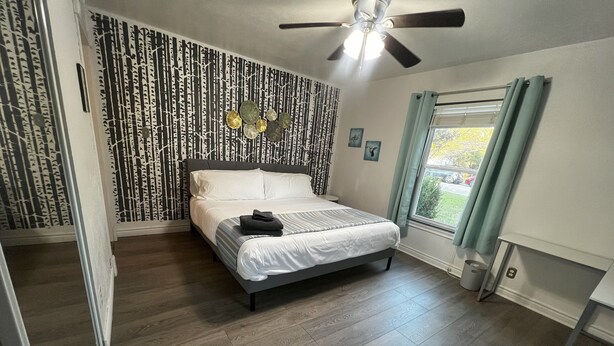 Een slaapkamer met een bed, een plafondventilator, een raam met gordijnen en een behang met patroon.