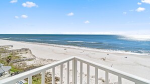 A beach view from a balcony with a wooden railing, sandy beach, and ocean. - Romar Place 903 (Orange Beach)