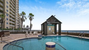 A pool area with a wooden gazebo, lounge chairs, and a tall building in the background. - Romar Place 903 (Orange Beach)