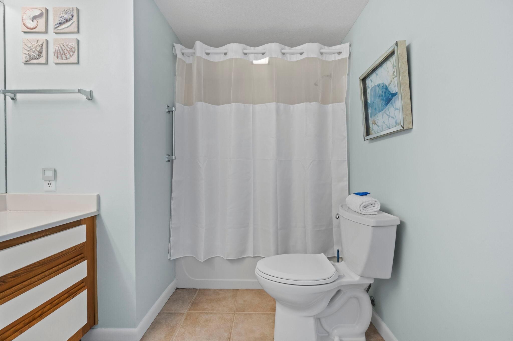 A bathroom with a toilet, a shower curtain, a sink, and a towel rack.