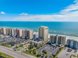 A coastal hotel complex with multiple high-rise buildings, a parking area, and a view of the ocean. - Romar Place 903 (Orange Beach)