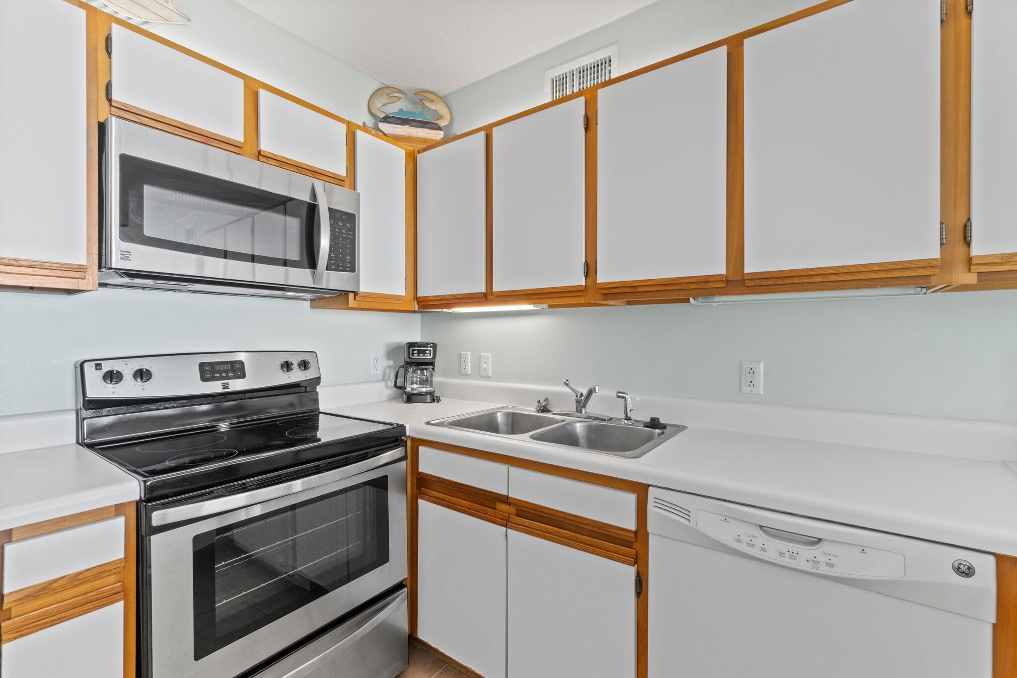 A compact kitchen with a microwave, stove, sink, and dishwasher.