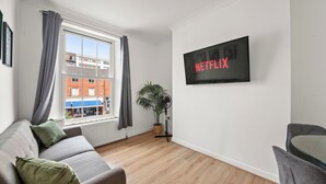 A modern living room with a grey sofa, a small table, and a wall-mounted TV displaying 'NETFLIX'.