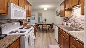 A kitchen with wooden cabinets, a white stove, a microwave, and a brick backsplash. - AT&T, Globe Life, Six Flags - Updated Comfy Home (Grand Prairie)