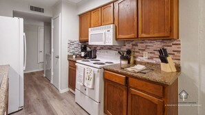 A kitchen with wooden cabinets, a white stove, a microwave, and a granite countertop. - AT&T, Globe Life, Six Flags - Updated Comfy Home (Grand Prairie)