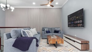 A modern living room with two grey sofas, a wooden coffee table, a TV mounted on the wall, and a ceiling fan. - Coastal Escape Tower Isle Beach Nearby (Tower Isle)