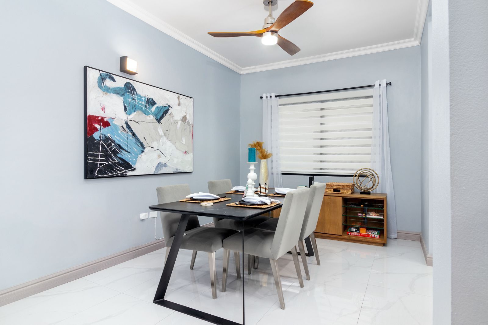 A dining area with a table set for four, a ceiling fan, and a large abstract painting on the wall.