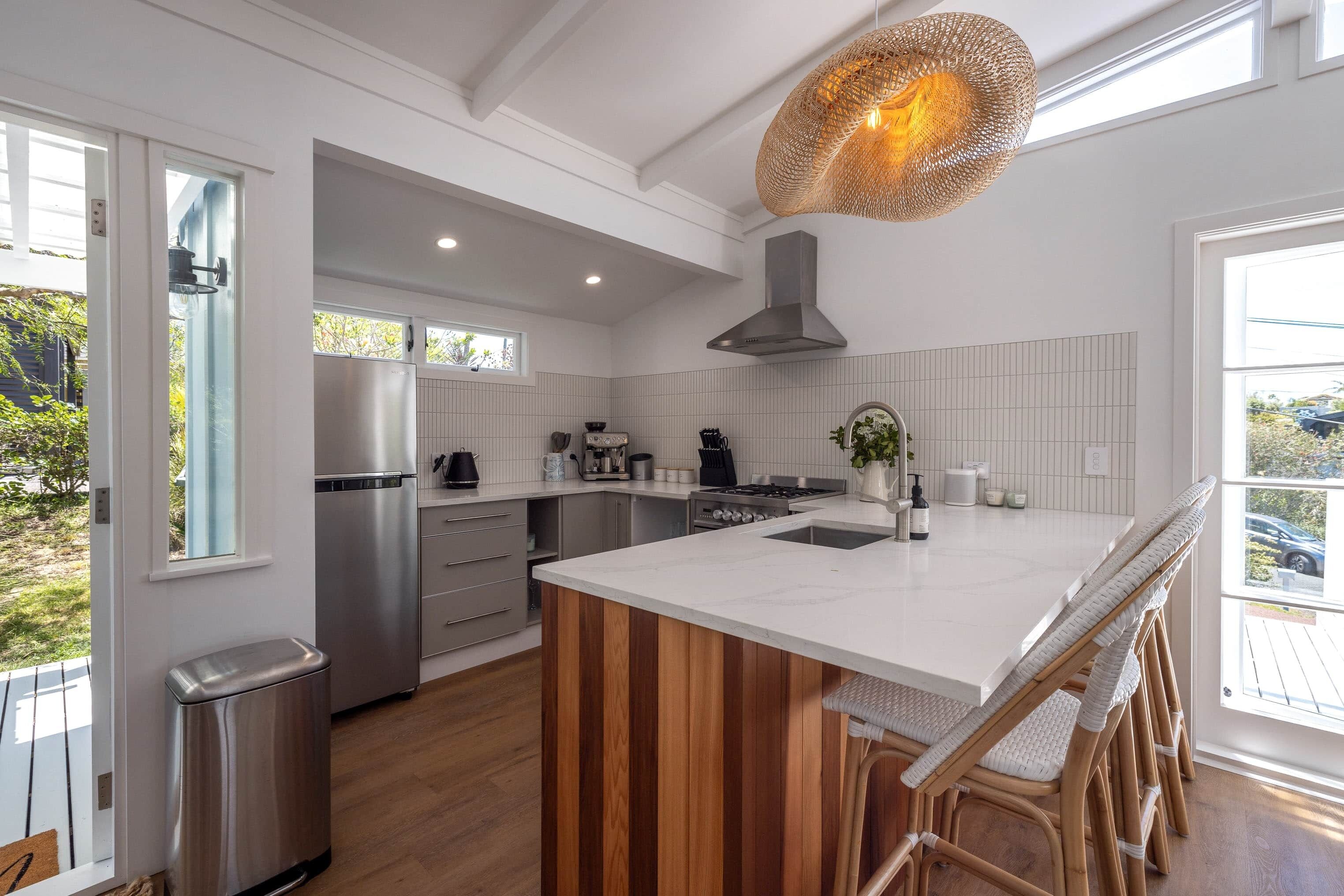 Une cuisine moderne dotée d’un grand îlot central, d’appareils électroménagers en acier inoxydable et d’un luminaire suspendu.