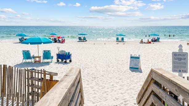 Une plage avec des parasols bleus, des chaises longues et une promenade en bois.