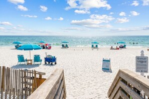 Une plage avec des parasols bleus, des chaises longues et une promenade en bois.